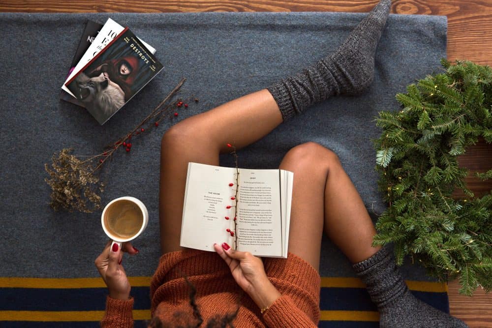 Female sitting on blanket with cup of coffee and book