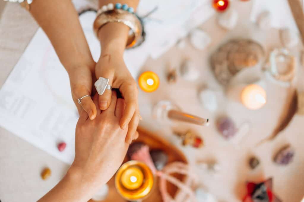 Vrouw houdt met twee handen de hand van andere vrouw vast. Kaarsen en kristallen op achtergrond